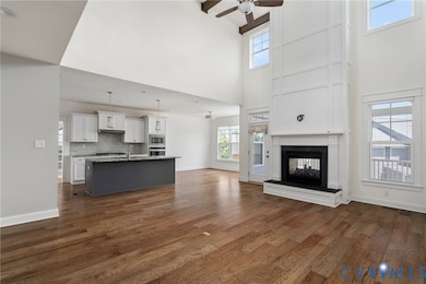 Unfurnished living room featuring a multi sided fireplace, dark wood-style flooring, a ceiling fan, and a towering ceiling