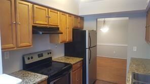 Kitchen featuring range with electric stovetop, under cabinet range hood, brown cabinetry, and freestanding refrigerator