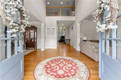 Entrance foyer with ornate columns, a towering ceiling, wood finished floors, baseboards, and a chandelier