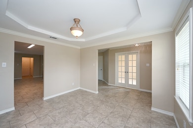 Spare room with a raised ceiling, healthy amount of natural light, french doors, crown molding, and light tile patterned floors