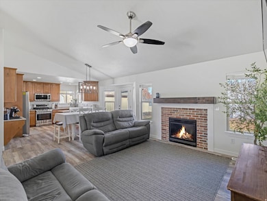 Living room featuring light wood-type flooring, lofted ceiling, a fireplace, ceiling fan, and a chandelier