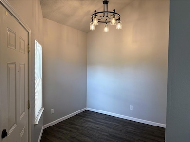 Empty room with dark wood finished floors, a textured ceiling, and a chandelier