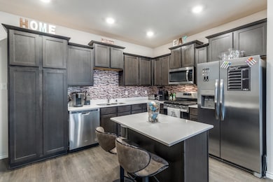 Kitchen featuring appliances with stainless steel finishes, tasteful backsplash, light wood-type flooring, a breakfast bar area, and recessed lighting