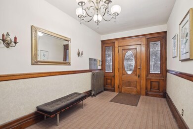 The main entry to the building is spacious and welcoming. Note the rich natural woodwork and the sidelight windows with leaded glass accents.