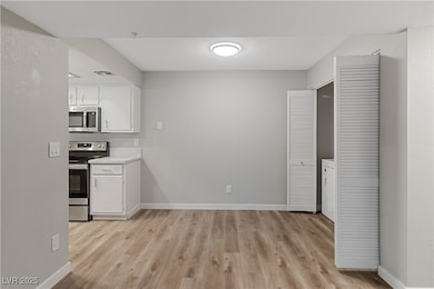 Dining area and Kitchen with appliances with stainless steel finishes, white cabinets, light wood-style flooring, and washer / clothes dryer