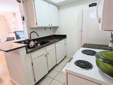 Kitchen featuring white appliances, track lighting, white cabinetry, light wood finished floors, and a peninsula