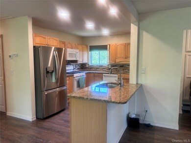 Kitchen with white appliances, dark stone countertops, dark wood-type flooring, a peninsula, and decorative backsplash