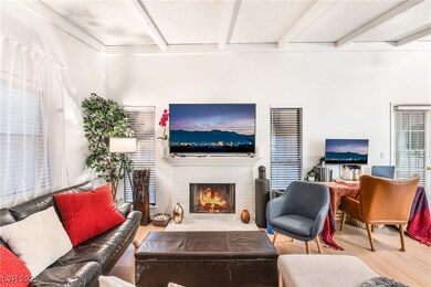 Living room with beamed ceiling, wood finished floors, a brick fireplace, and a textured ceiling