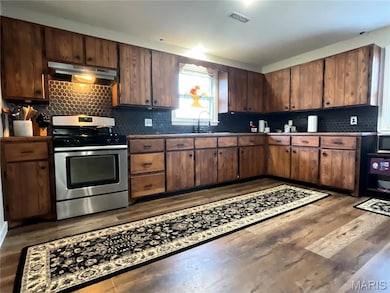 Kitchen featuring stainless steel range with gas stovetop, decorative backsplash, under cabinet range hood, and dark wood-style floors