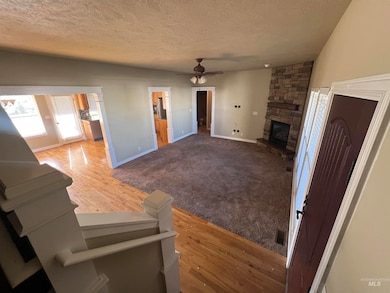 Unfurnished living room featuring a textured ceiling, a stone fireplace, light wood flooring, a ceiling fan, and light carpet