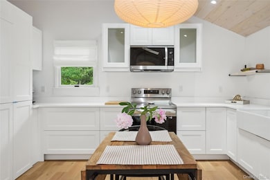 Kitchen with white cabinets, stainless steel appliances, light wood-style floors, vaulted ceiling, and glass insert cabinets