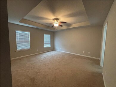 Carpeted spare room with a tray ceiling, a ceiling fan, and baseboards