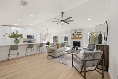 Living area with lofted ceiling, light wood-style flooring, a fireplace, a chandelier, and a ceiling fan