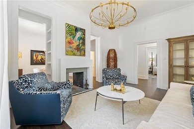 Living area with a chandelier, a fireplace with raised hearth, built in shelves, wood finished floors, and crown molding