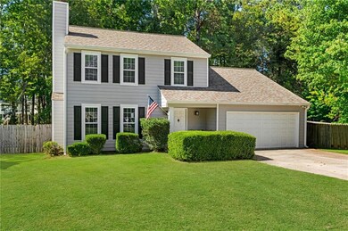 View of front of property featuring a chimney, concrete driveway, a shingled roof, a garage, and view of wooded area