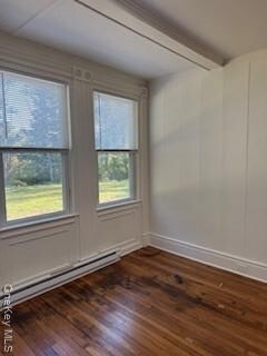 Bedroom featuring dark wood flooring, a baseboard heating unit, beamed ceiling, and a decorative wall