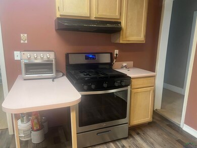 Kitchen with stainless steel gas range, under cabinet range hood, wood finished floors, light countertops, and light brown cabinetry