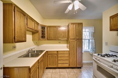 Kitchen featuring white gas range, ceiling fan, light tile flooring, and sink