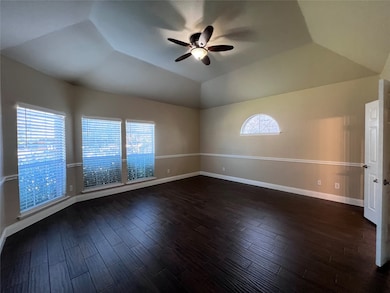 Downstairs primary bedroom featuring dark wood-style flooring, ceiling fan, and vaulted ceiling