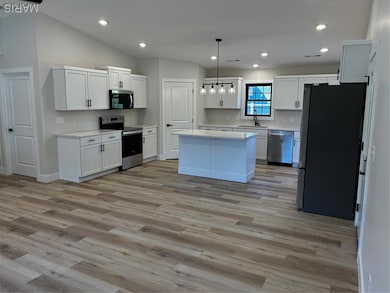 Kitchen with appliances with stainless steel finishes, recessed lighting, decorative light fixtures, white cabinets, and light wood finished floors