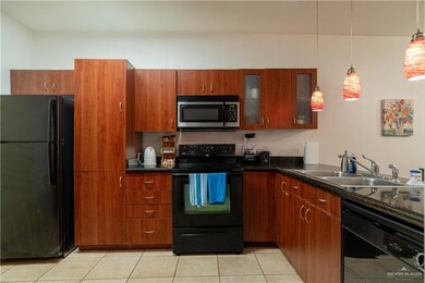 Kitchen with black appliances, a sink, brown cabinetry, and dark countertops