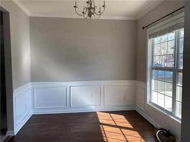 Unfurnished dining area featuring a chandelier, crown molding, dark wood finished floors, and wainscoting