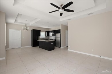 Kitchen with appliances with stainless steel finishes, a raised ceiling, dark cabinets, ceiling fan with notable chandelier, and open floor plan