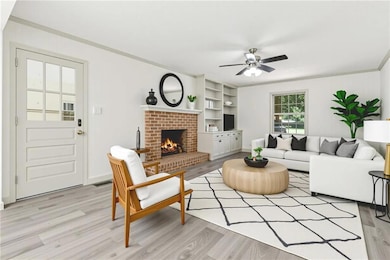 Living area with crown molding, light wood-type flooring, a brick fireplace, and ceiling fan