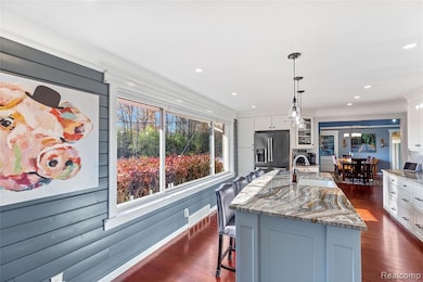 Kitchen with light high end granite countertops, a breakfast bar area, white cabinets, hanging light fixtures, remote control blinds, motion sensor under cabinet lighting, and recessed lighting