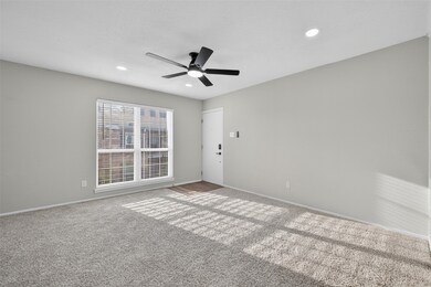 Bright and airy room with neutral walls and carpet, featuring a large window for natural light, recessed lighting, and a modern ceiling fan.