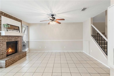 Unfurnished living room featuring a fireplace, light tile patterned floors, stairs, ceiling fan, and a textured ceiling