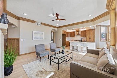 Living room with arched walkways, light wood-style floors, ceiling fan, crown molding, and recessed lighting