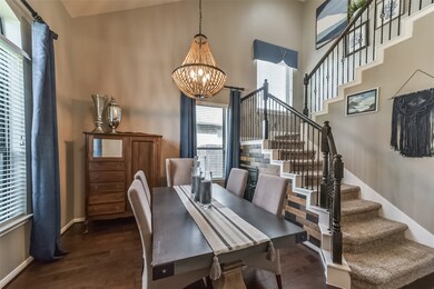 This is a modern dining space with a stylish chandelier, adjacent to an elegant staircase with ornate metal balusters. The room features neutral tones, natural light, and a warm, inviting atmosphere.