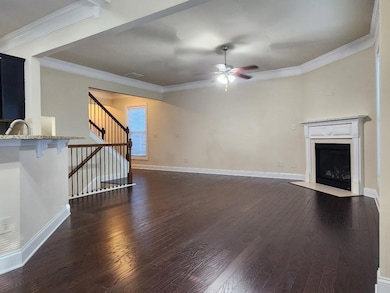 Unfurnished living room with ceiling fan, dark wood finished floors, a fireplace with flush hearth, ornamental molding, and stairs