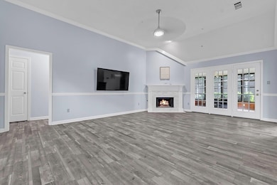 Unfurnished living room featuring lofted ceiling, a ceiling fan, crown molding, wood finished floors, and a lit fireplace