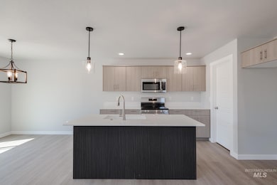 Kitchen featuring a center island with sink, decorative light fixtures, appliances with stainless steel finishes, light wood-style floors, and light brown cabinetry