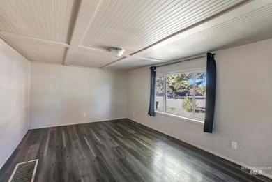 Empty room featuring dark wood-type flooring and beam ceiling