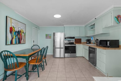 Kitchen with stainless steel appliances, a sink, open shelves, light tile patterned floors, and crown molding