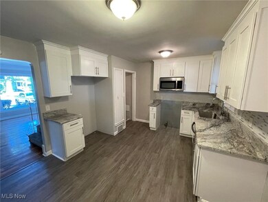 Kitchen with light stone countertops, white cabinetry, sink, and dark hardwood / wood-style flooring