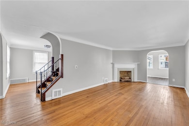 Unfurnished living room with arched walkways, light wood-style flooring, ornamental molding, a fireplace, and stairs