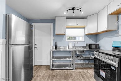 Kitchen with stainless steel appliances, light wood-style flooring, and white cabinets