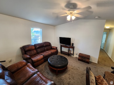 Living room featuring ceiling fan, carpet, and vaulted ceiling