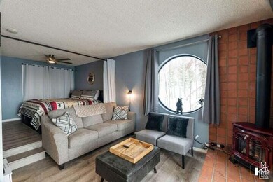 Living area featuring a wood stove, a textured ceiling, ceiling fan, and light wood-style flooring