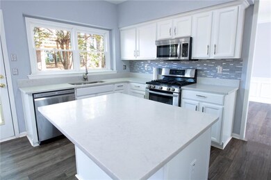 Kitchen featuring appliances with stainless steel finishes, white cabinets, dark wood-style floors, a center island, and backsplash