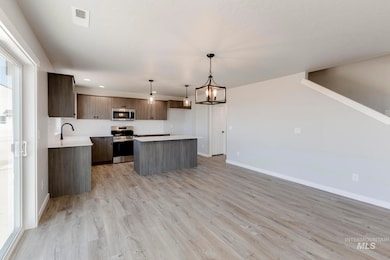 Kitchen with light countertops, a kitchen island, hanging light fixtures, appliances with stainless steel finishes, and a chandelier