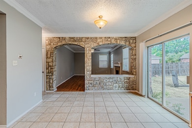 Unfurnished room featuring ornamental molding, tile patterned flooring, a textured ceiling, healthy amount of natural light, and arched walkways