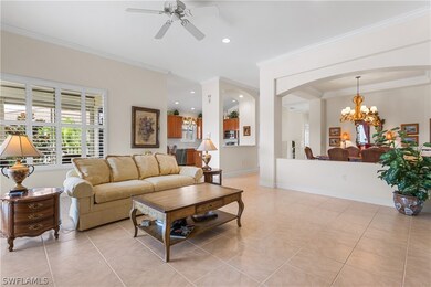 Living room featuring ornamental molding, ceiling fan with notable chandelier, and light tile patterned floors