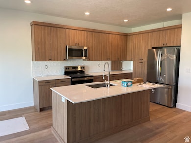 Kitchen featuring stainless steel appliances, recessed lighting, light countertops, brown cabinetry, and light wood-type flooring
