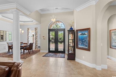 Foyer entrance with french doors, crown molding, decorative columns, arched walkways, and light tile patterned flooring