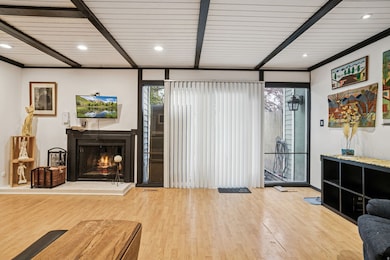 Living area with a lit fireplace, light wood finished floors, recessed lighting, and a wood ceiling with exposed beams